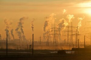 Silhouette de lignes électriques et de fumée industrielle au coucher du soleil, mettant en évidence les thèmes de la pollution et de l'énergie.