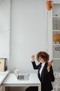 Une femme d'affaires aux cheveux bouclés célèbre son succès lors d'un appel téléphonique dans un bureau moderne avec un ordinateur portable.