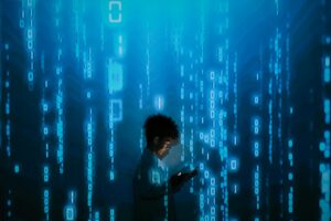 Silhouette d'une personne utilisant un smartphone entourée de projections de codes binaires numériques.